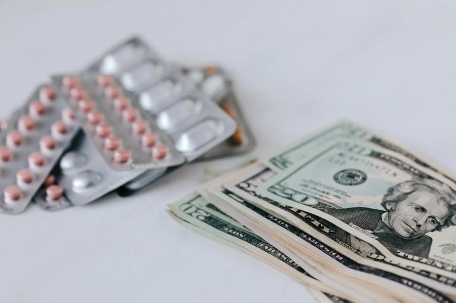 Different pill blisters near pile of American dollar banknotes