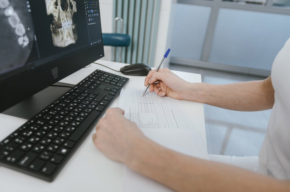 person writing on a document in front of a desktop