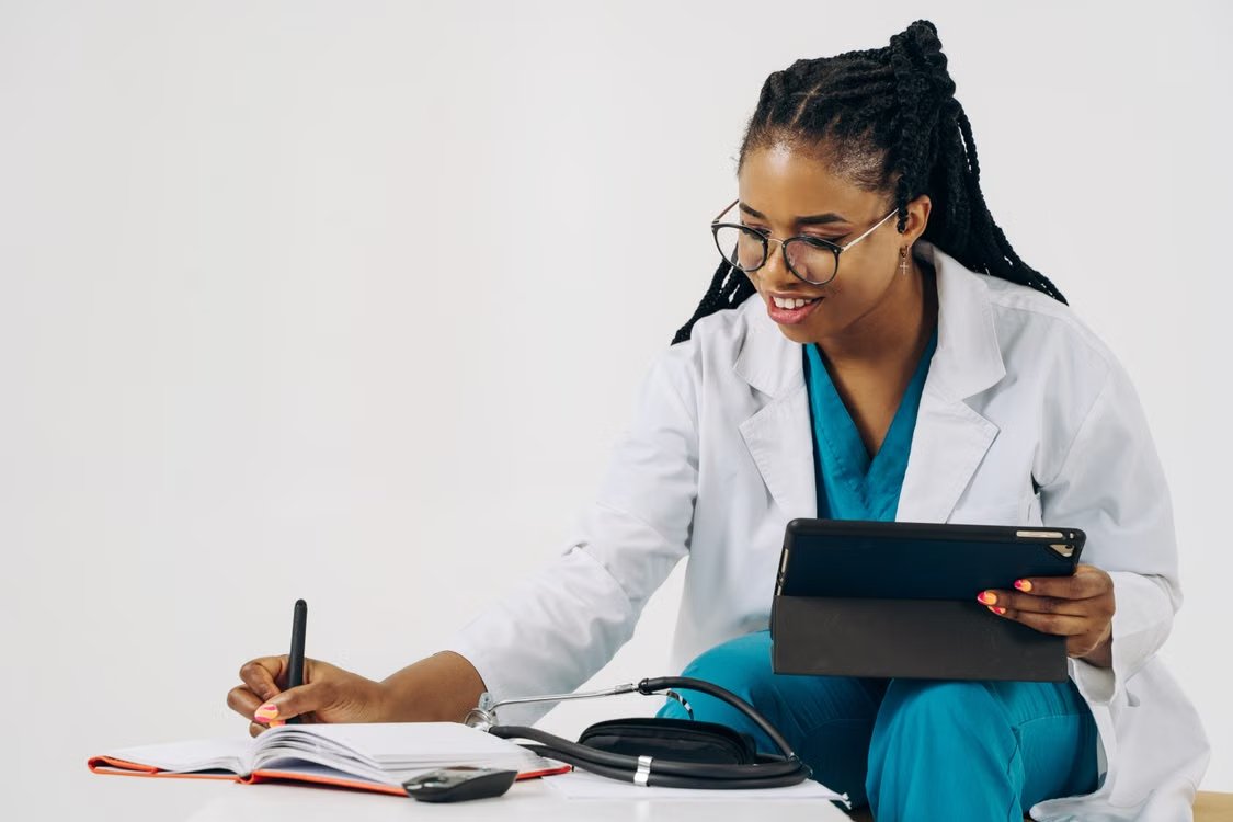 Smiling female doctor in scrubs using tablet and taking notes in a healthcare setting